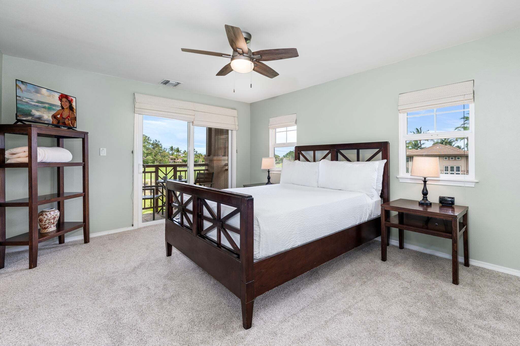 A bedroom with a bed, a nightstand, a ceiling fan, a TV, and a window with a view.