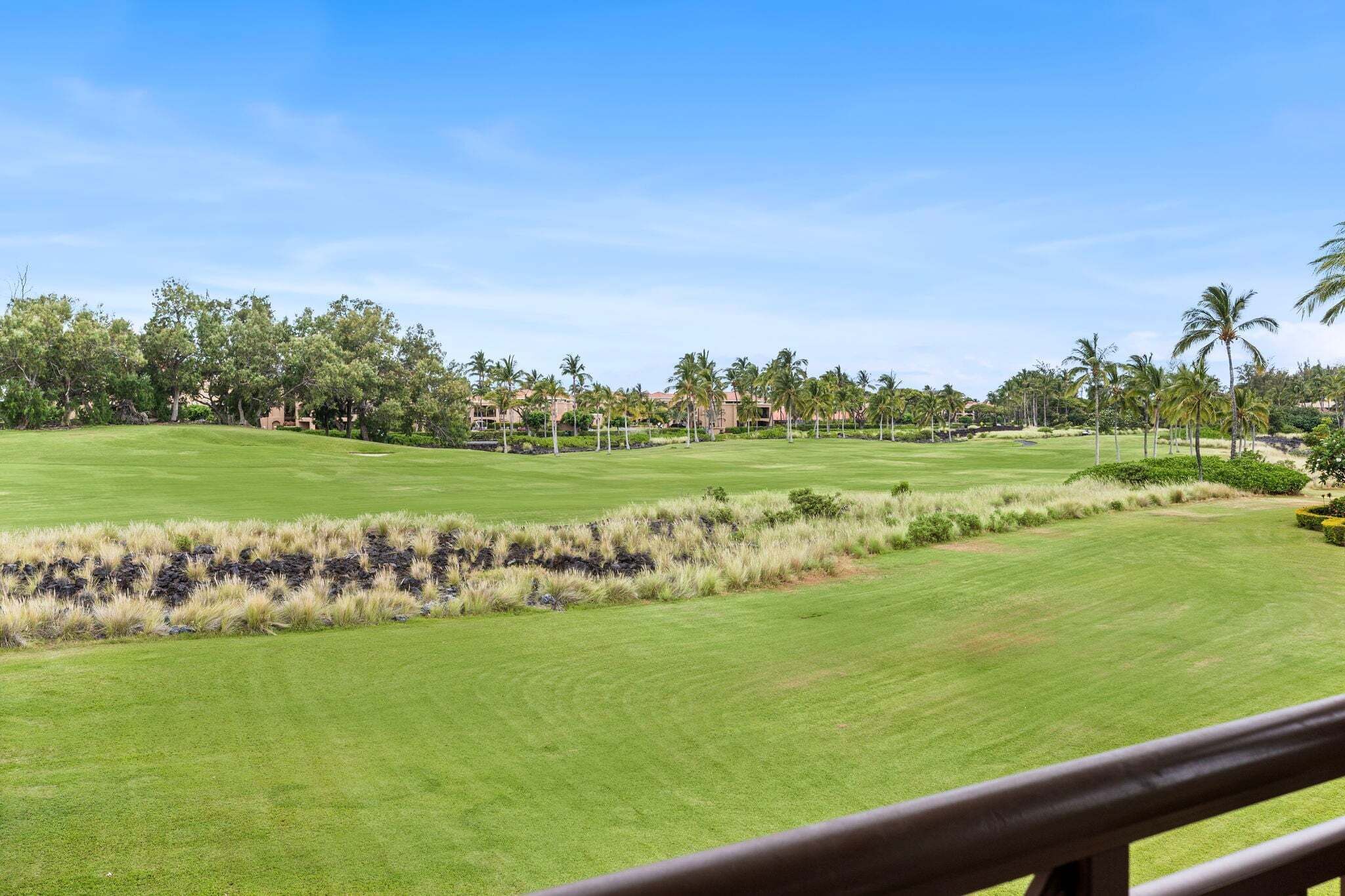 Un campo de golf con vista despejada al fairway, búnkeres de arena y un complejo de edificios en la distancia.