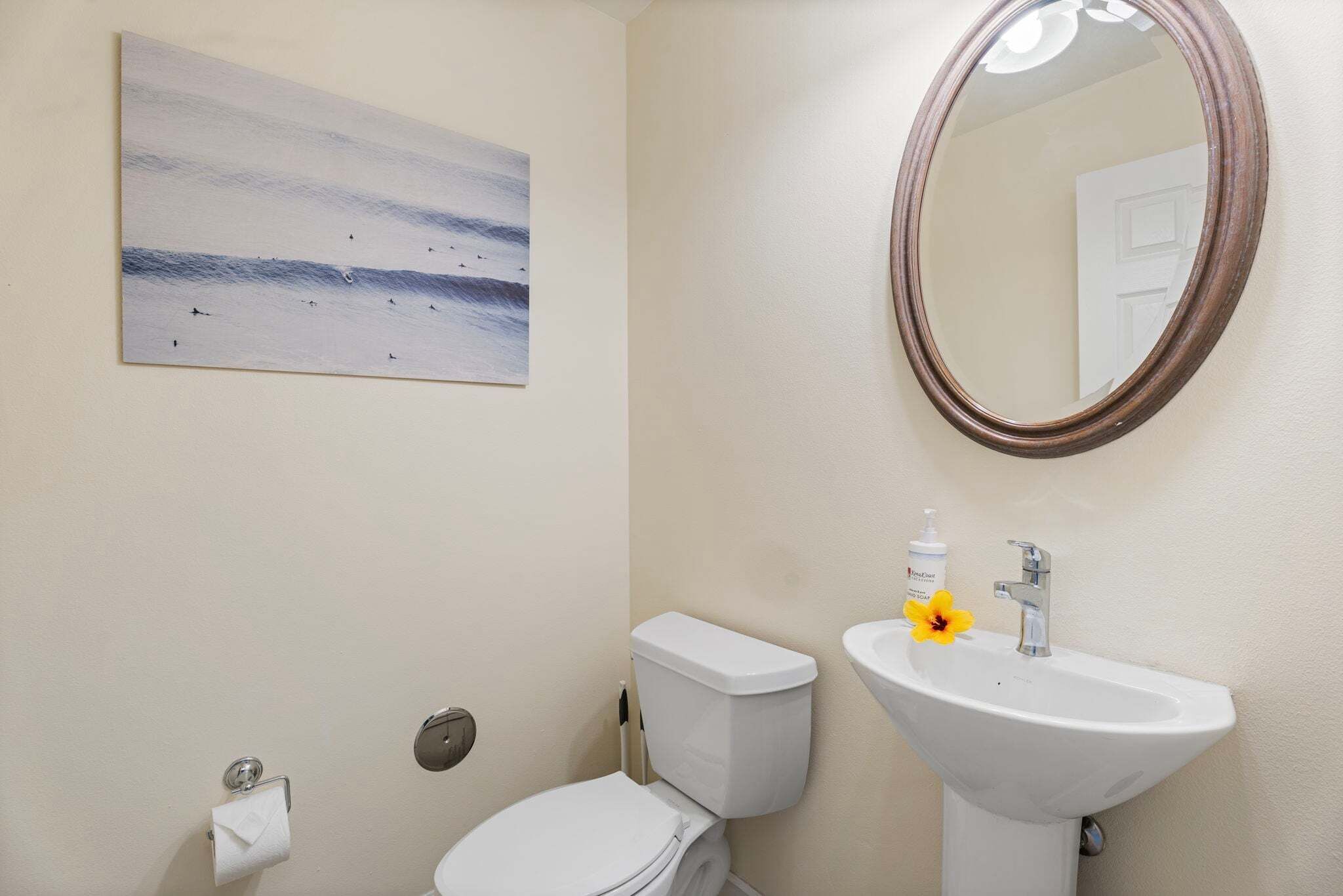 A bathroom with a toilet, sink, mirror, and a painting on the wall.