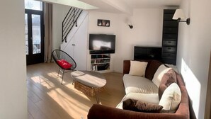 Ein modernes Wohnzimmer mit einer Couch, einem Sessel, einem Fernseher und einer Treppe.