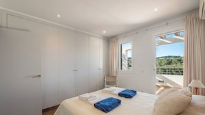Une chambre à coucher avec un lit, une armoire, une fenêtre avec des rideaux et une vue sur la verdure à l’extérieur.