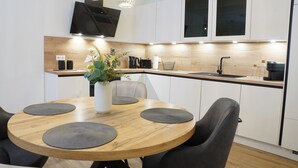 A modern kitchen with a wooden dining table, black chairs, and a built-in oven. - Küste33/8 - North Sea time on the dyke. Sauna. Beach chair. Balcony. (Tossens)