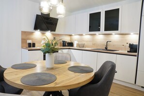 A modern kitchen with a wooden dining table, black chairs, and a built-in oven. - Küste33/8 - North Sea time on the dyke. Sauna. Beach chair. Balcony. (Tossens)