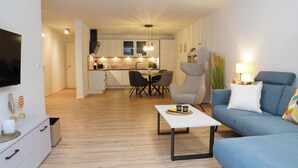 A modern living room with a blue sofa, a coffee table, and a TV on a white cabinet. - Küste33/8 - North Sea time on the dyke. Sauna. Beach chair. Balcony. (Tossens)