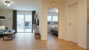 A modern living room with a sofa, a coffee table, and a dining area. There is a kitchen visible in the background with a refrigerator and a sink. - Küste33/8 - North Sea time on the dyke. Sauna. Beach chair. Balcony. (Tossens)