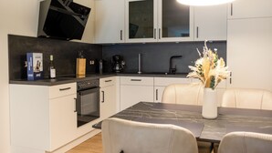 Une cuisine moderne avec des meubles blancs, un plan de travail noir et un coin repas comprenant une table en marbre et des chaises en cuir.