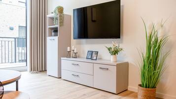 A modern living room with a flat-screen TV mounted on the wall, a white cabinet with drawers, a round table, and a large potted plant.