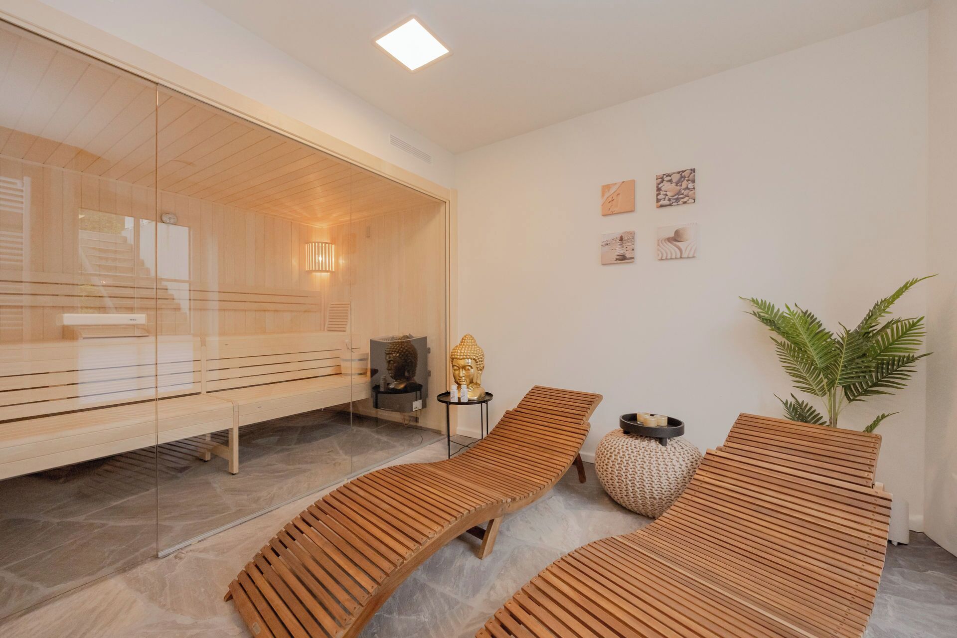 A modern spa room with wooden loungers, a glass sauna, and a small Buddha statue.