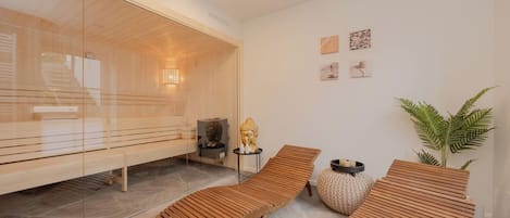 A modern spa room with wooden loungers, a glass sauna, and a small Buddha statue.