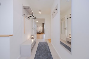 A hallway with a grey carpet, white walls, and a door leading to a room with a grey sofa. - Villa Schlossallee Rügen - thatch on the golf course. Sauna. Sea view. (Lohme)