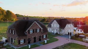 A residential area with two houses, one with a thatched roof and the other with a stone facade, surrounded by a well-maintained lawn and a curved driveway. - Villa Schlossallee Rügen - thatch on the golf course. Sauna. Sea view. (Lohme)