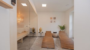 A spa room with wooden loungers, a bench, a small table with a Buddha statue, a potted plant, and a wall-mounted heater. - Villa Schlossallee Rügen - thatch on the golf course. Sauna. Sea view. (Lohme)