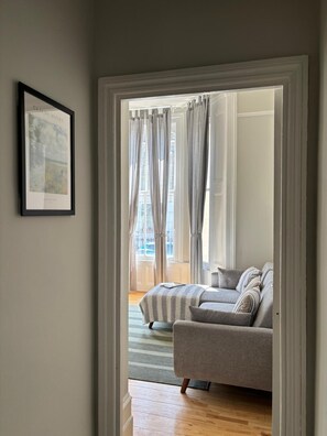 A room with a grey sofa, a framed picture on the wall, and a view through a doorway to an outdoor area with a striped rug. - Flat Clapham Junction one bedroom, living room. Kitchen, washing machine,  WiFi. (London)