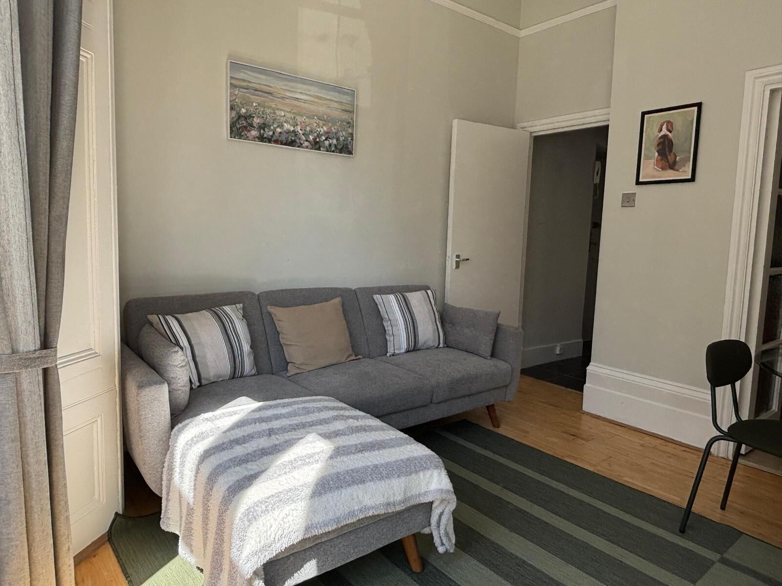 Un salon avec un canapé gris, un plaid à rayures et un tableau accroché au mur.