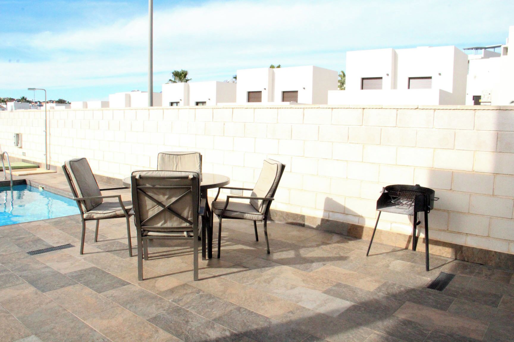 An outdoor patio with a pool, a barbecue grill, and a seating area with chairs and a table.