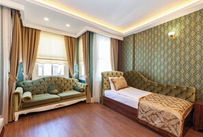 Ein Zimmer mit einem grünen Sofa, einem Bett mit gemustertem Überwurf, Holzboden und Tapete mit Muster.
