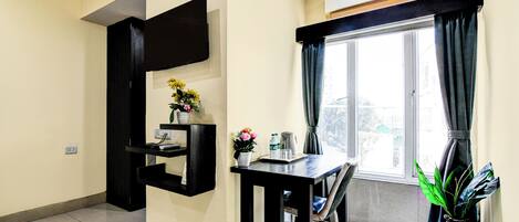 Una sala de estar moderna con un televisor de pantalla plana montado en la pared, una mesa de comedor con sillas, una planta en maceta y una ventana con cortinas.