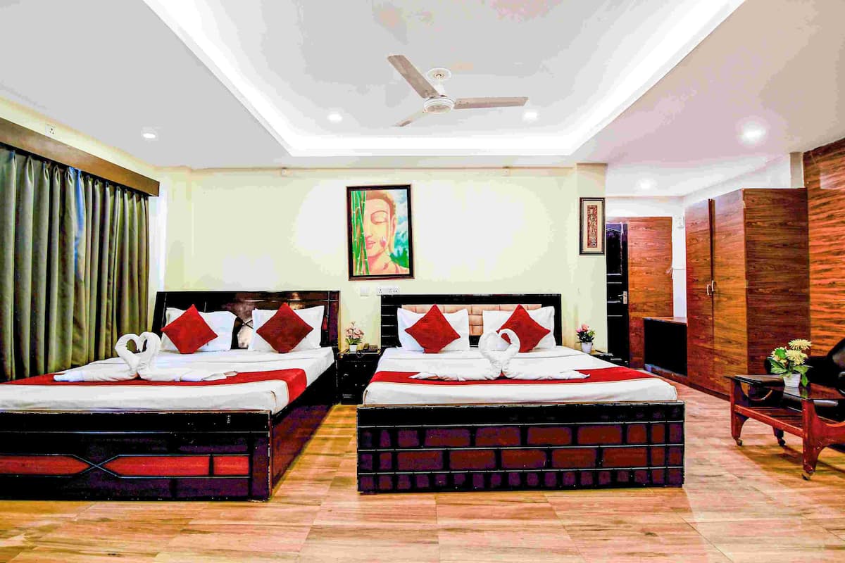 A hotel room with two beds, a ceiling fan, a painting on the wall, and a wooden wardrobe.
