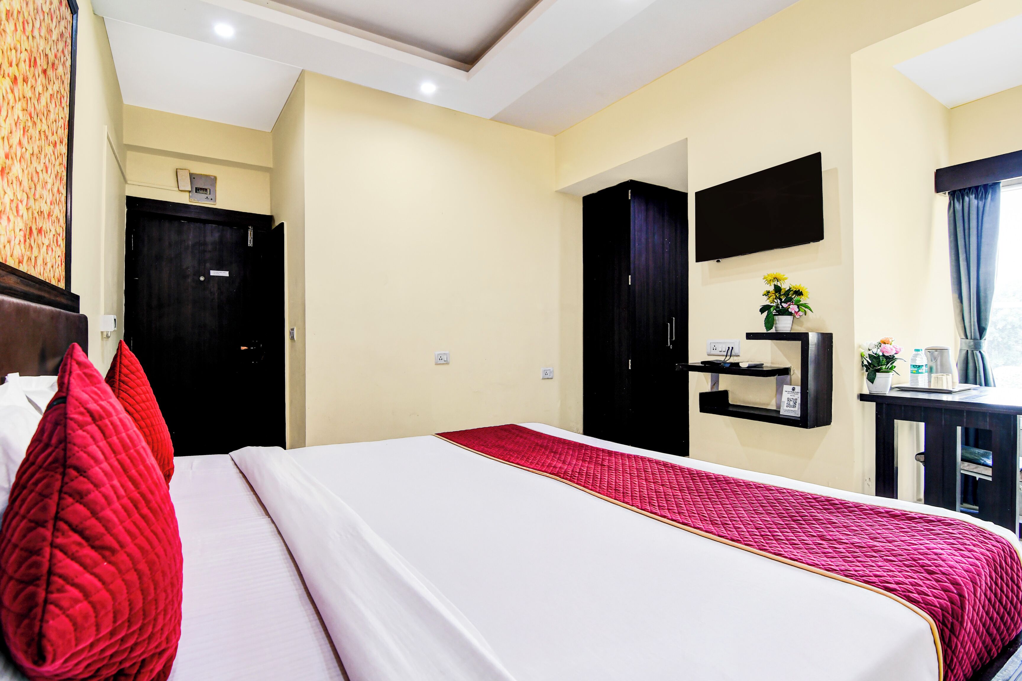 A hotel room with a bed, a desk, a TV, and a door.