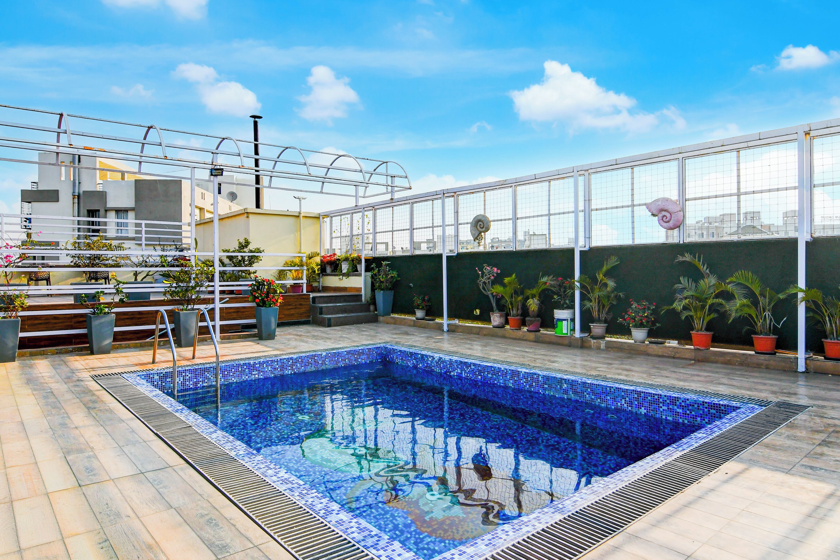 A rooftop swimming pool with a tiled edge, surrounded by potted plants and a metal railing.