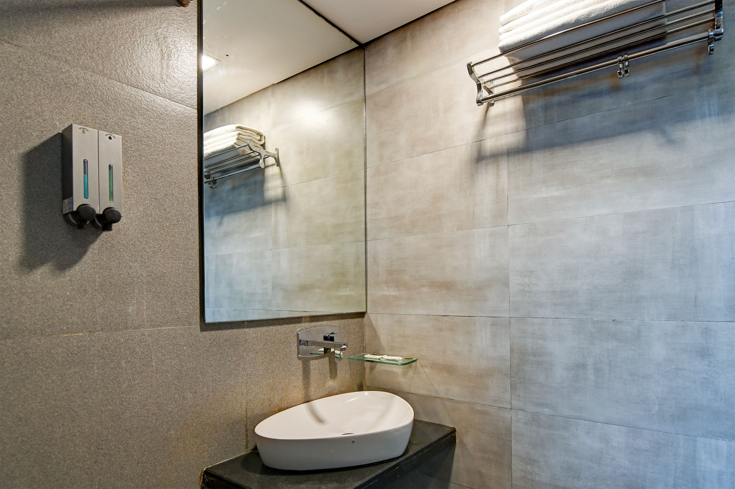 Un bagno moderno con un lavandino bianco, uno specchio, un porta asciugamani e un dispenser per sapone.