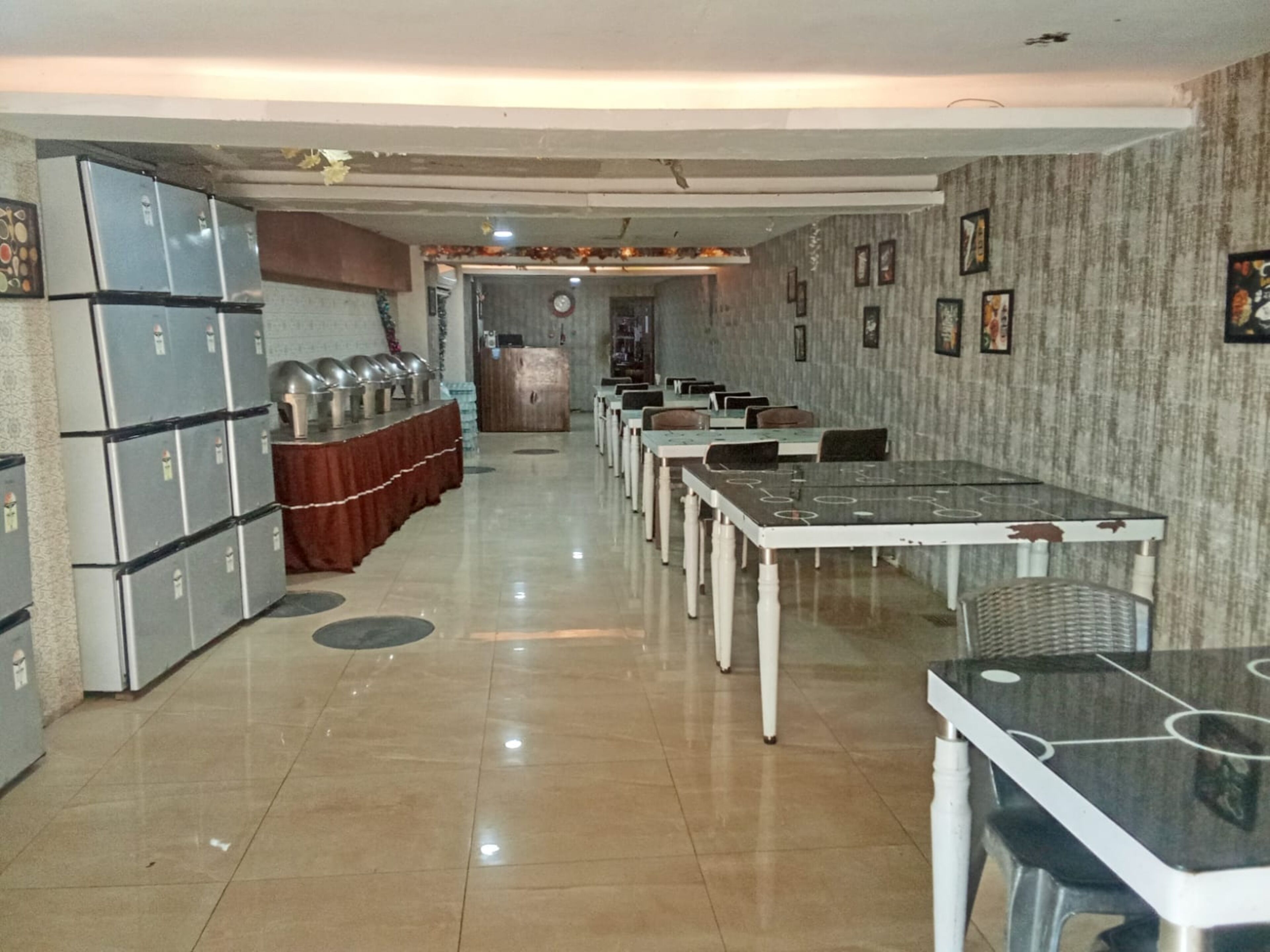 Uma área de refeições com mesas, cadeiras, um buffet com recipientes de comida e uma geladeira.