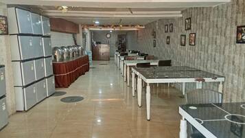 Uma área de refeições com mesas, cadeiras, um buffet com recipientes de comida e uma geladeira.
