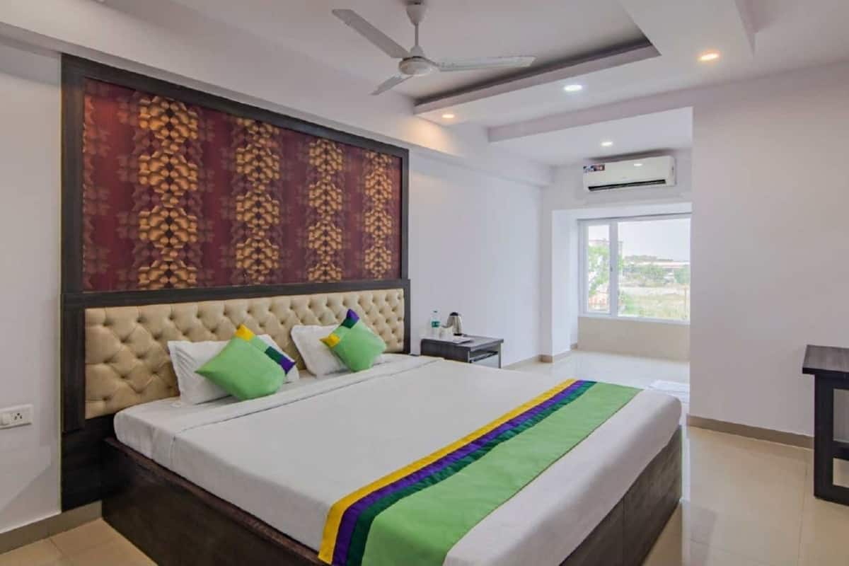 A hotel room with a large bed, a ceiling fan, an air conditioning unit, and a window with a view.