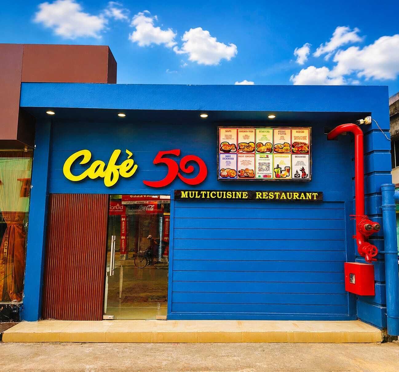 Un edificio azul con un letrero que dice 'Café 59 MULTICUISINE RESTAURANT' y una pizarra de menú sobre la entrada.