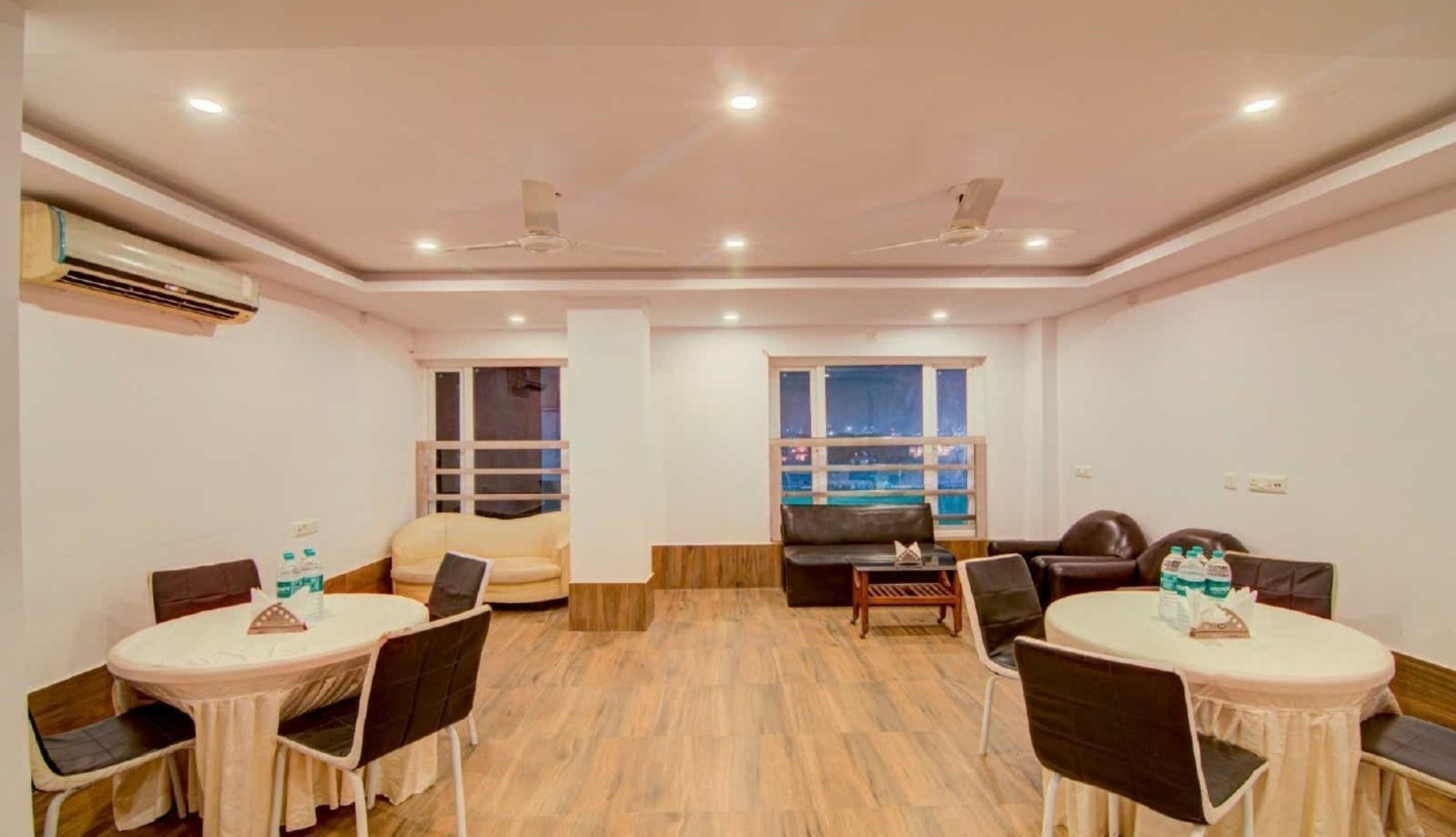 Un salón de conferencias con dos mesas redondas, sillas, un sofá y un ventanal con vistas a la ciudad.
