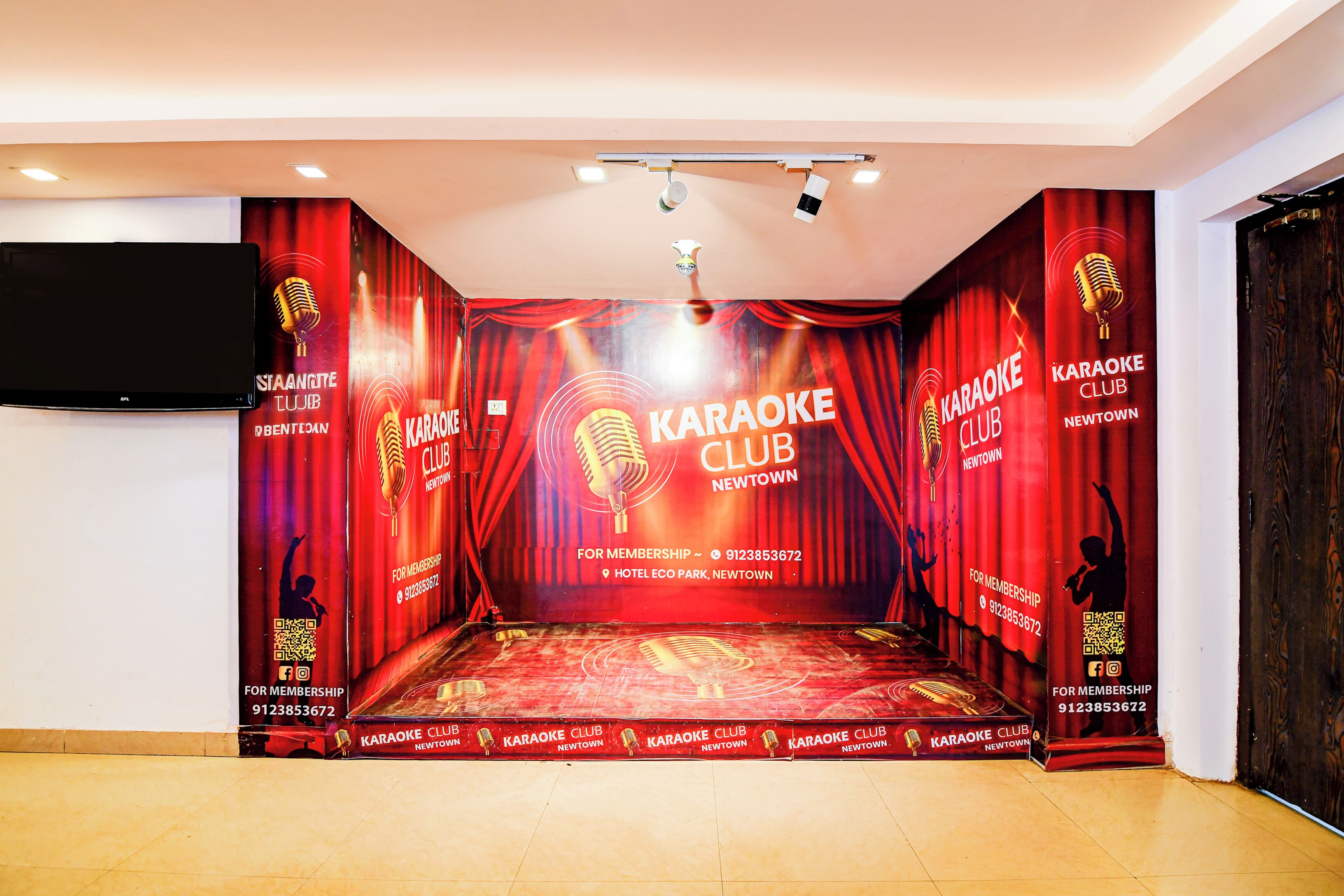 A karaoke club interior with a stage, red curtains, and promotional banners.