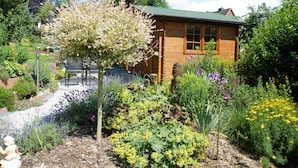A wooden cabin with a green roof surrounded by a garden with various plants and flowers. - Apartment Balogh - Welcome to the Harz Mountains - because your vacation starts here ✓ (Osterode am Harz)