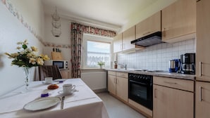 A kitchen with wooden cabinets, a stove, and a window with curtains. - Apartment Balogh - Welcome to the Harz Mountains - because your vacation starts here ✓ (Osterode am Harz)