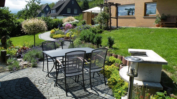 A patio with a table and chairs, surrounded by a garden with various plants and flowers. - Apartment Balogh - Welcome to the Harz Mountains - because your vacation starts here ✓ (Osterode am Harz)