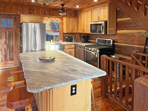 A kitchen with wooden cabinetry, a stainless steel refrigerator, a microwave, a stove, and a granite countertop. - Bear Cove - rustic mountainside cabin with incredible view + free train tix (Bryson City)