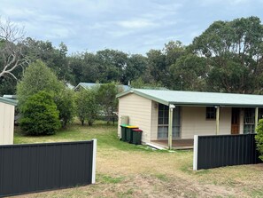 A small, single-story house with a green roof, a porch, and a fenced yard. - 700m to Surf Beach•Relaxed Family Coastal Escape for 5•Linen provided (Venus Bay)