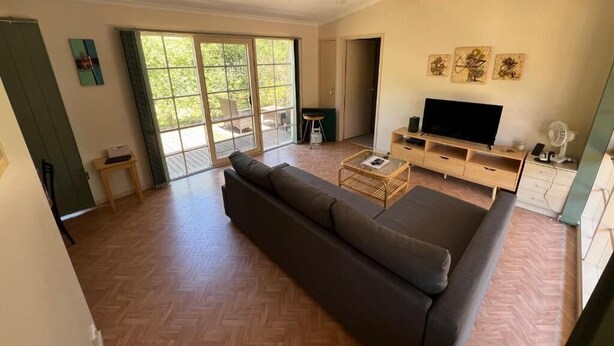 A spacious living room with a large sofa, a television, and a sliding glass door leading to a balcony. - 700m to Surf Beach•Relaxed Family Coastal Escape for 5•Linen provided (Venus Bay)