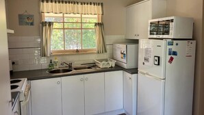 A compact kitchen with white cabinets, a double sink, a stove, a microwave, and a refrigerator. - 700m to Surf Beach•Relaxed Family Coastal Escape for 5•Linen provided (Venus Bay)