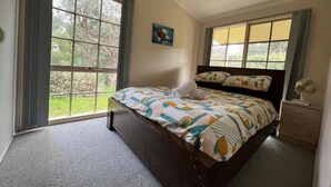 A bedroom with a large window, a bed with patterned bedding, a bedside table, and a wall-mounted fan. - 700m to Surf Beach•Relaxed Family Coastal Escape for 5•Linen provided (Venus Bay)