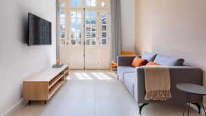 Una sala de estar moderna con un sofá gris, una mesita de madera, una pequeña mesa redonda y un televisor fijado a la pared.