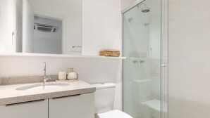 Un baño moderno con ducha de vidrio, lavamanos blanco y encimera de granito, y un inodoro.