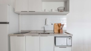 Una cocina con gabinetes blancos, una encimera, un microondas y una tabla de cortar de madera con utensilios.