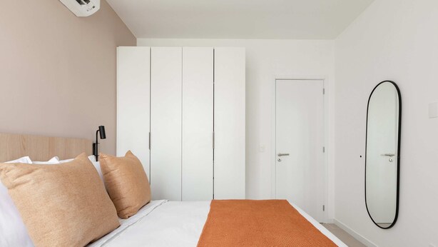 Un dormitorio con cama, armario blanco y espejo en la pared.