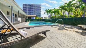 A rooftop pool area with lounge chairs, a swimming pool, and a view of a high-rise building. - A boutique, renovated coastal retreat featuring fully equipped condos w/kitchen, minutes walking to the beach & restaurants, exciting amenities like a heated pool, BBQ Grill, hammock and fun yard games. Centrally located, minutes to Pompano Beach! (Pompano Beach)