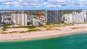 A coastal cityscape with high-rise buildings, a beach, and clear skies. - A boutique, renovated coastal retreat featuring fully equipped condos w/kitchen, minutes walking to the beach & restaurants, exciting amenities like a heated pool, BBQ Grill, hammock and fun yard games. Centrally located, minutes to Pompano Beach! (Pompano Beach)
