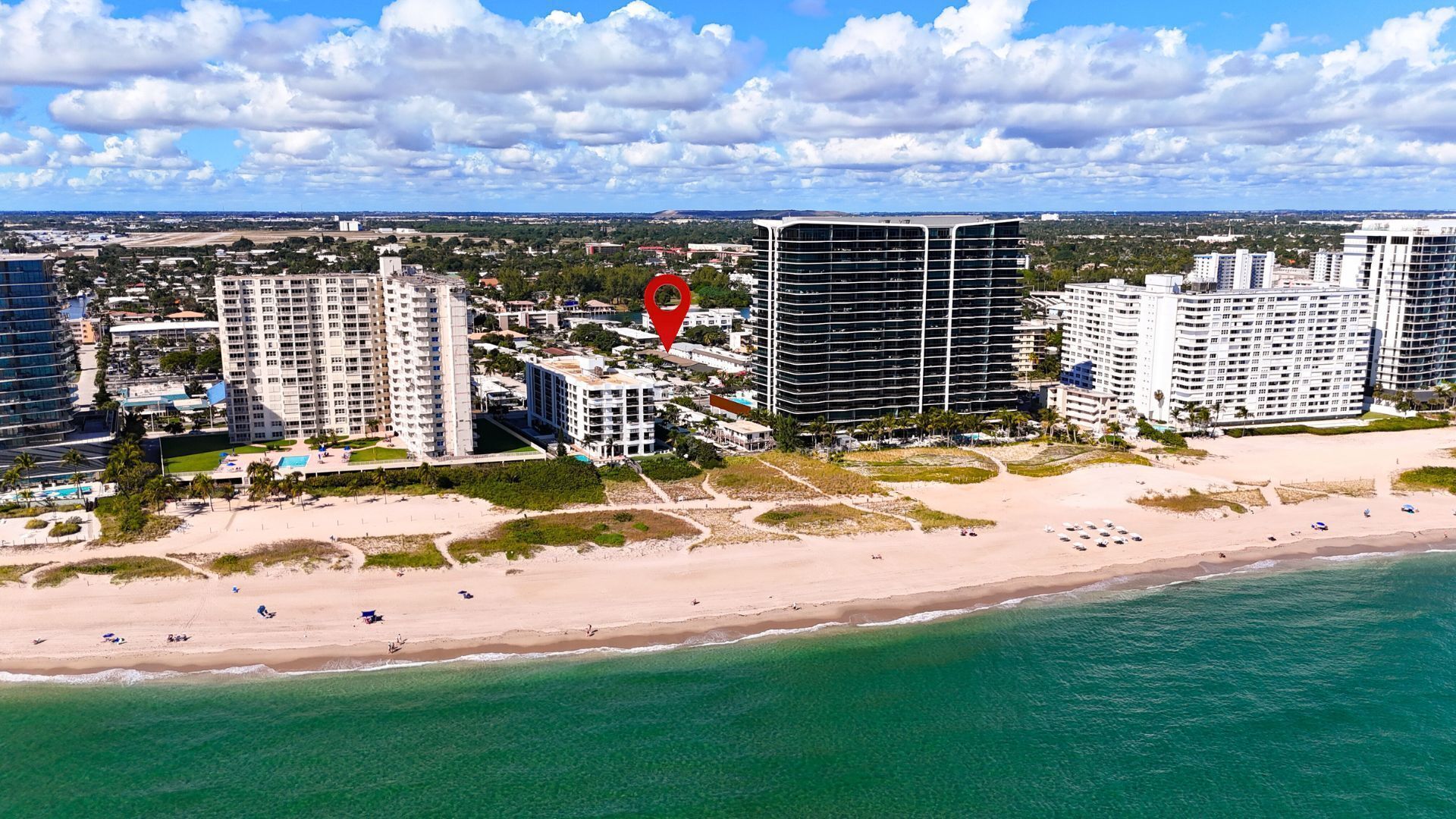 An aerial view of a coastal city with high-rise buildings, a beach, and a clear sky.
