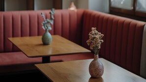 A restaurant interior with a wooden table, a vase with flowers, and a red booth. - Waidmannhof (Merano)