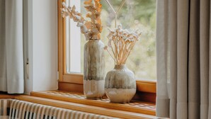 A window seat with a view of greenery, a vase with dried flowers, and a lamp. - Waidmannhof (Merano)