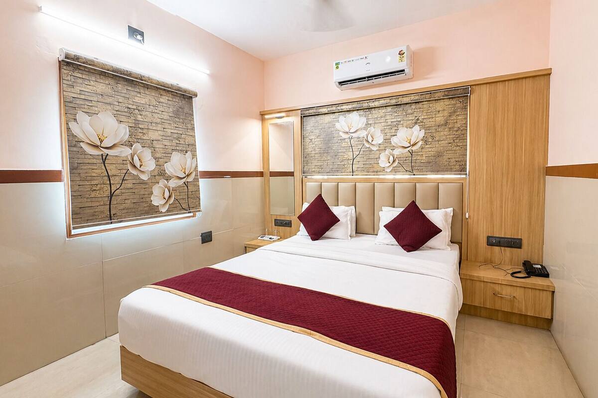 A hotel room with a bed, a nightstand, an air conditioning unit, and a window with a floral design.