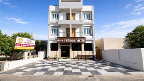 A multi-story hotel named 'Hotel Shreenidhi' with a checkered floor outside, a signboard indicating A/C and non-A/C rooms, and a clear blue sky. - GoHotels Shreenidhi Dwarka (Dwarka)
